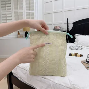 Detailed view of a light green fabric drawstring bag with floral embroidery and tag.