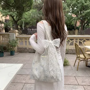 Detailed view of floral embroidered tote bag with a large lace bow carried by a model