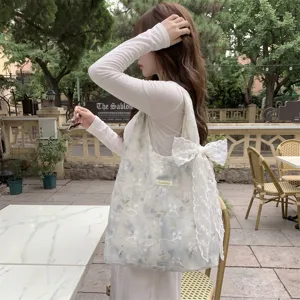 Floral embroidery tote bag with lace bow shown in a casual lifestyle outdoor setting.