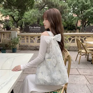Side detail of floral embroidery tote bag with a large white lace bow shoulder strap
