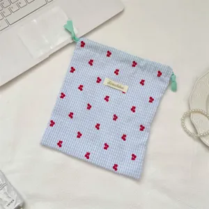 Bolsa de cordón de cuadros azul y blanco con bordado de cerezas rojas en entorno moderno