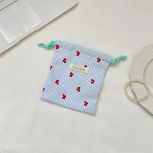 Primer plano de una bolsa de cordón vichy azul con bordado de pequeñas cerezas rojas