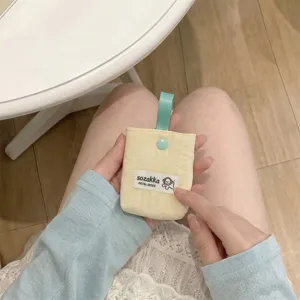 Detail showing a soft cream yellow quilted earphone storage pouch held in hands