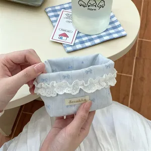Détail d'un panier de rangement en tissu bleu avec dentelle blanche et motifs nœuds.