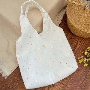Detailopname van een crème canvas schoudertas met een roze en blauw polka dot patroon