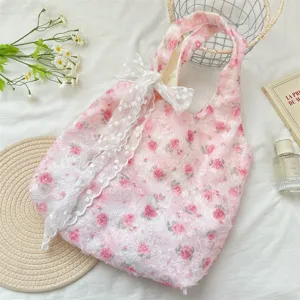 Detail view of a pink rose floral tote bag with a white lace bow accessory.