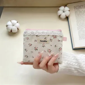 Gros plan d'une main tenant une petite pochette fleurie avec étiquette de marque Sozakka.
