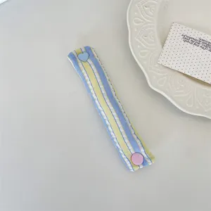 Primo piano del fermacavo in tessuto a righe macaron con chiusura a bottone a pressione a cuore