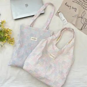 Two checkered canvas tote bags in a lifestyle setting with a laptop and flowers.