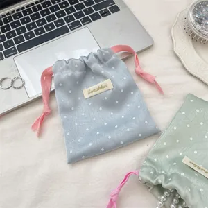 Close-up of a macaron blue polka dot satin drawstring bag with pink cords on a desk
