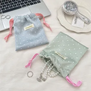 Close-up detail of macaron polka dot satin drawstring pouch with a pearl necklace.