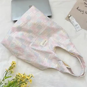 High-angle detail view of a pink and blue checkered canvas tote bag with lifestyle props.