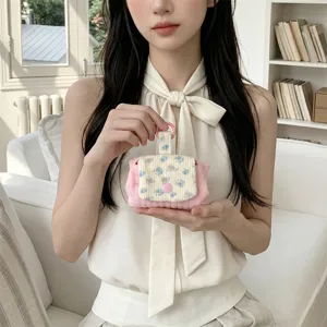 Close-up of a pink quilted mini pouch with floral flap held by a model in soft light