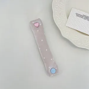 Primo piano di un morbido organizzatore per cavi a pois con bottone a cuore rosa.
