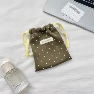 Close-up of olive green satin drawstring pouch with white polka dots and logo detail.