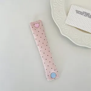 Dettaglio di un ferma cavo in tessuto a pois rosa con bottone a pressione a cuore