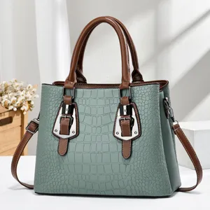 Close-up of sage green embossed crocodile handbag with brown leather handles and buckles.