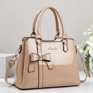 Elegant nude patent leather handbag featuring a chic bow detail and gold-tone hardware accents.