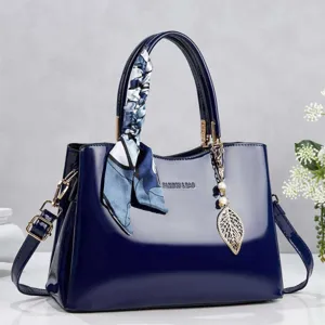Close-up of a navy blue patent leather handbag with a decorative silk scarf and leaf charm