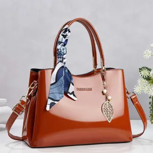 Elegant reddish-brown patent leather handbag with decorative scarf and gold leaf charm
