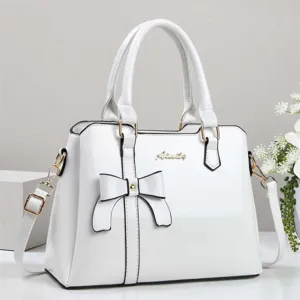 Detailed view of elegant white patent leather handbag with bow detail and gold logo accent