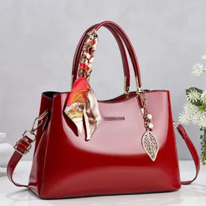 Detailed view of a red patent leather handbag featuring a decorative silk scarf and leaf charm.