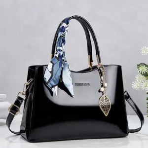 Detailed view of an elegant black patent leather handbag with a silk scarf and leaf charm