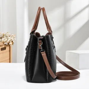 Side profile of a stylish black crocodile embossed handbag with brown handles and strap