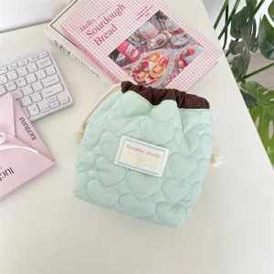 Detalle de bolsa de cordón acolchada con corazones verde menta para cosméticos en el escritorio