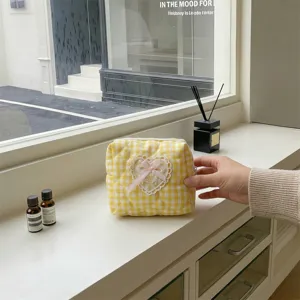 Quilted cosmetic pouch detail featuring yellow gingham fabric, cute heart lace patch and pink bow.