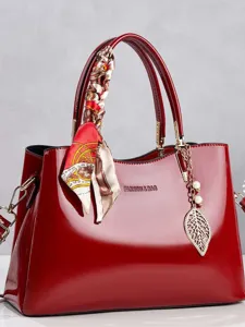 Elegant red patent leather handbag with decorative scarf and gold leaf pendant