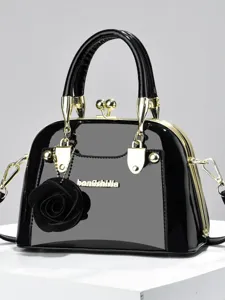 Borsa a mano a conchiglia in pelle verniciata nera con ciondolo rosa e dettagli dorati chic.
