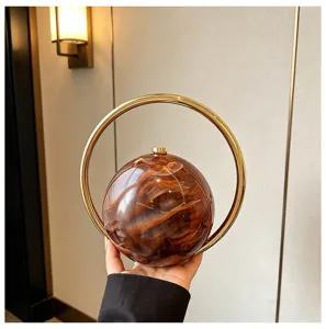 Detailopname van de ronde avondtas van bruin marmer acryl met gouden ringhandgreep.