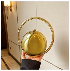 Close-up detail van de gouden metalen bolvormige avondtas met een cirkelvormig handvat.