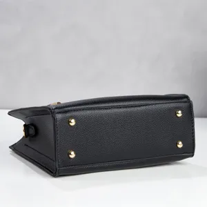 Black leather handbag bottom close-up detail with four metal feet and side hook for women.