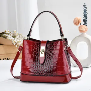 Détail de sac seau rouge vernis gaufré croco, fermeture à serrure élégante et bandoulière.
