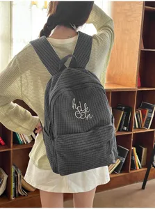 Close-up detail of a dark grey plaid student backpack with white embroidery lettering.