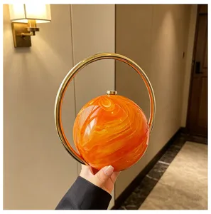 Detailopname van de stijlvolle ronde oranje acryl avondtas met een gouden ringhandvat.