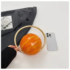 Detail van acryl avondtas in oranje marmerlook met gouden ringhandvat voor dames.