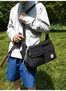 Close-up detail of a black nylon messenger bag worn outdoors, featuring multiple utility pockets.