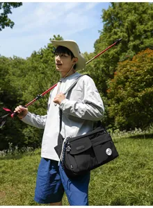 Outdoor lifestyle detail shot of a male model wearing a black nylon crossbody messenger bag.