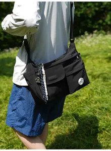 Black nylon crossbody messenger bag outdoor detail view showing strap and front pocket design