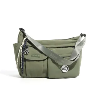 Olive green nylon crossbody bag featuring multiple front pockets, wide strap and cute charm.