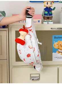 Détail du sac de poitrine imprimé pomme avec pendentif en peluche et fermeture éclair.