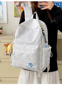 Backpack detail view showing embroidered blue flower and letter pattern on stylish fabric.