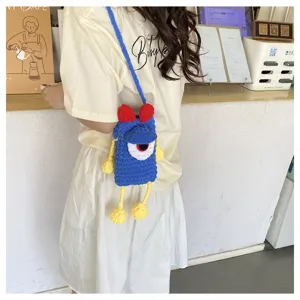 Detailed view of the cute handmade knitted blue monster phone crossbody bag in cafe setting.