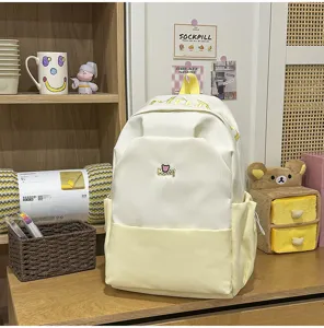 Detail view of stylish white yellow contrast backpack with cute embroidered bear and letter design.