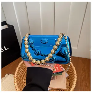 Detailansicht der glänzenden blauen Acryl-Clutch mit luxuriösen Goldperlen-Kettenriemen.