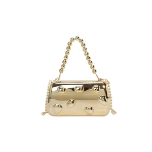 Goldfarbene metallische Abendtasche mit Perlenhenkel und feiner Kettenriemen im Detail.