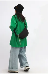 Black woven crescent crossbody bag detail view worn with green top and denim jeans.